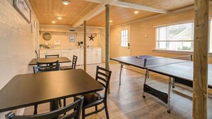 A cozy room with a ping pong table, wooden ceiling, and a kitchen area in the background.