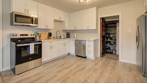 A modern kitchen with white cabinets, stainless steel appliances, and a wooden floor.