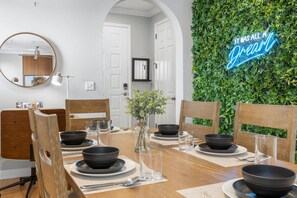 A dining area with a wooden table set for four, surrounded by wooden chairs. A neon sign on the wall reads "IT WAS ALL A DREAM." - SOHO Getaway! 3BR Jacuzzi, Gym AND Game-room (Tampa)