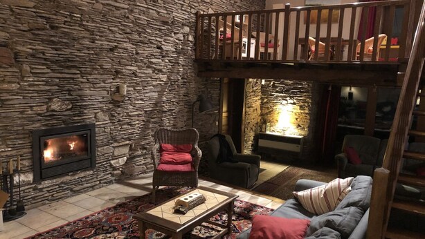 Ein gemütliches Wohnzimmer mit Steinwand, Kamin, einer Couch, einem Couchtisch und einem Balkon.