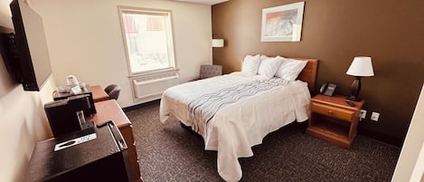 Habitación de hotel con cama, escritorio, silla, teléfono, lámpara y ventana.