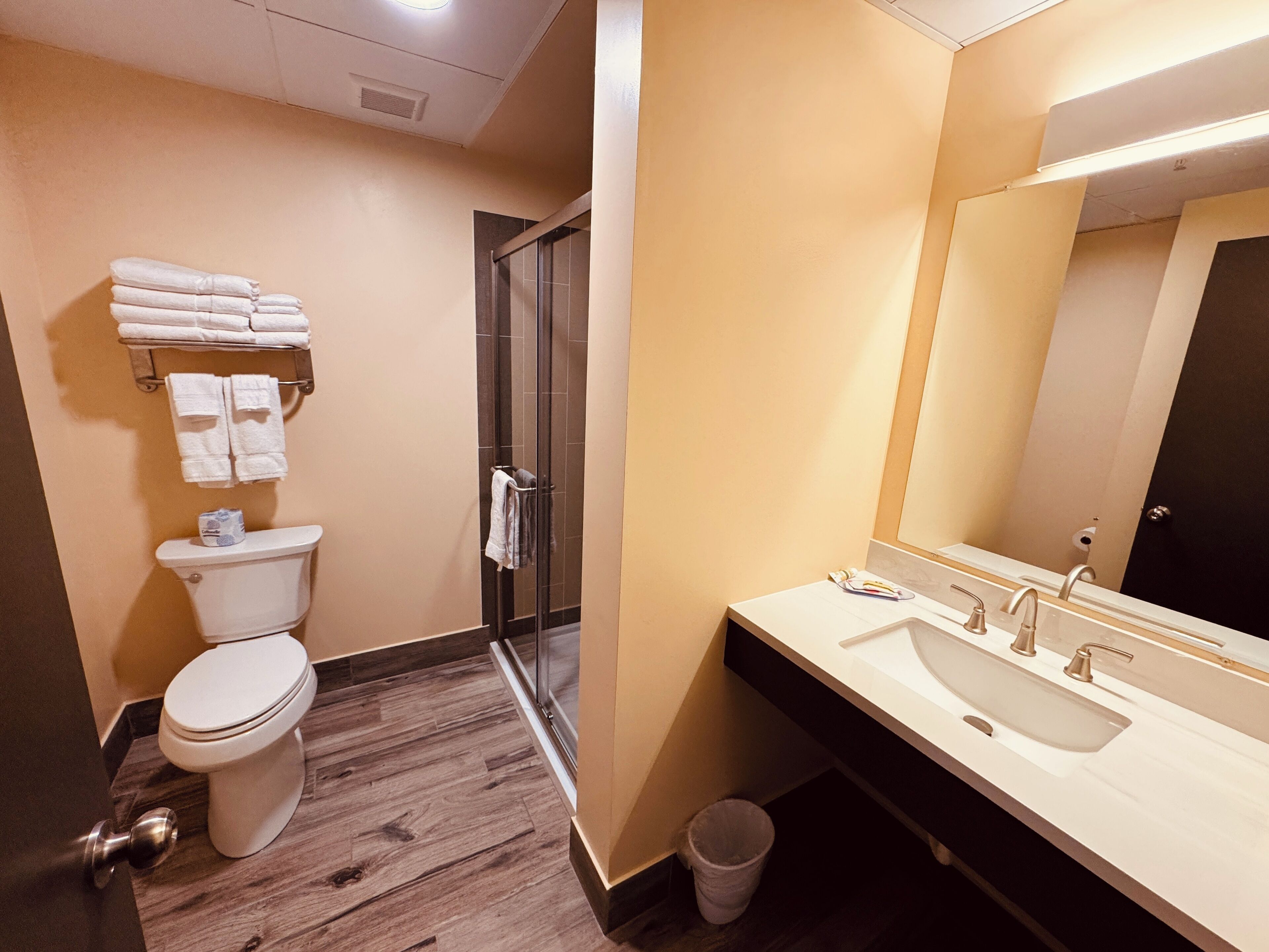Une salle de bain moderne comprenant des toilettes, une douche en verre, un lavabo avec un miroir et des serviettes soigneusement pliées.