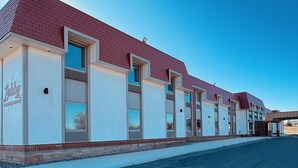 A row of hotel rooms with a red roof and white walls, a covered entrance, and a clear blue sky.
