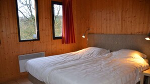 Une chambre aux murs lambrés, avec un lit, une fenêtre avec un rideau et une lampe fixée au mur.