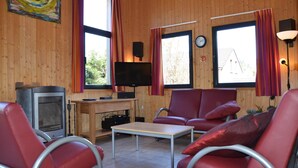 Une pièce chaleureuse avec un décor intérieur en bois, une télévision, une cheminée et des fauteuils rouges.