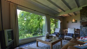 A cozy living room with a large window, a stone fireplace, and a television. - Modern chalet with a view (Humain)