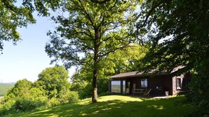 A rustic cabin with a large tree in front, a grassy lawn, and a scenic view of the landscape. - Modern chalet with a view (Humain)
