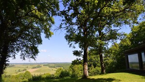 A view of a countryside landscape with a building featuring large windows, surrounded by trees and open fields. - Modern chalet with a view (Humain)