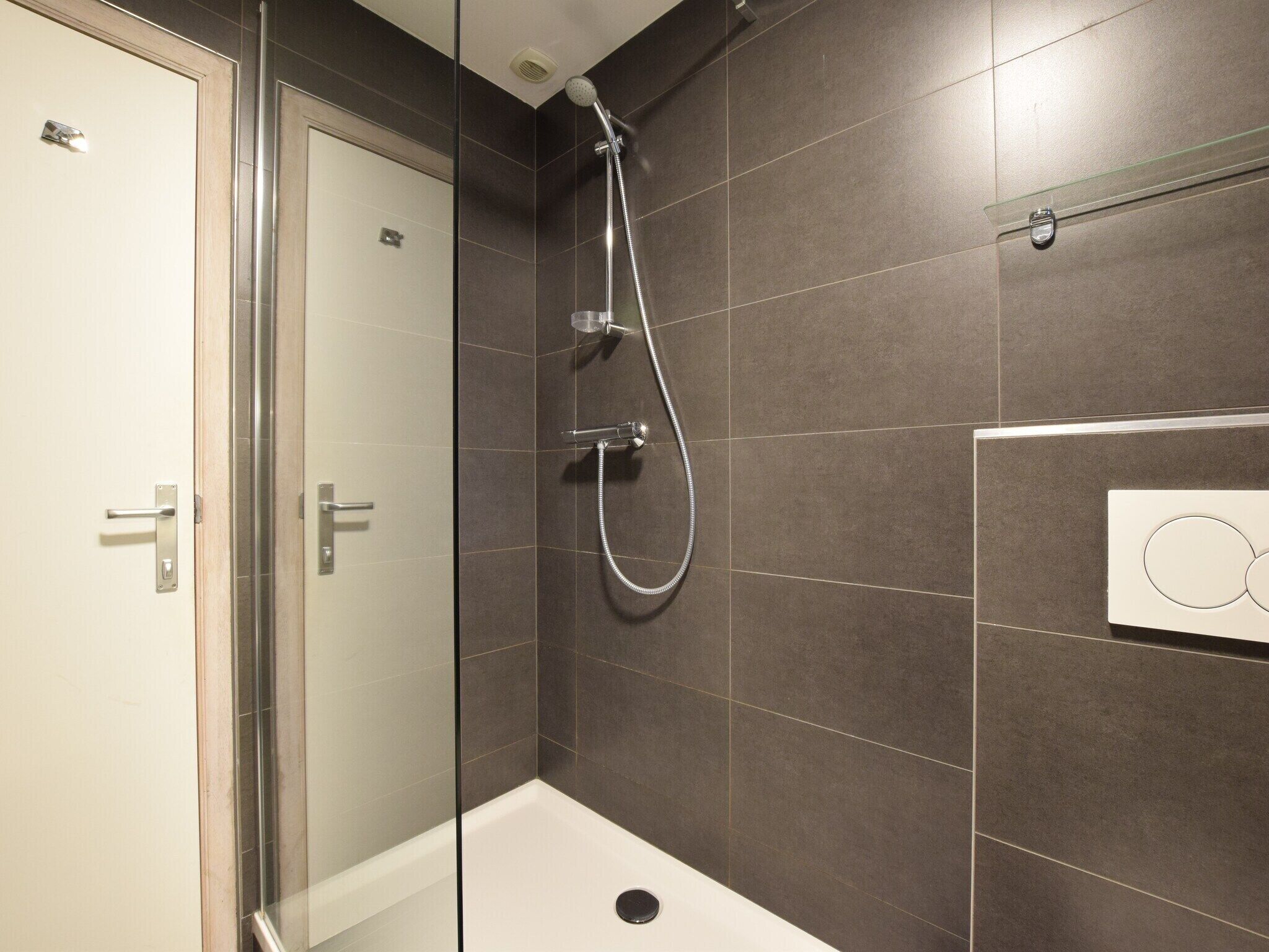 A modern bathroom with a glass shower enclosure, a white bathtub, and dark tiled walls.