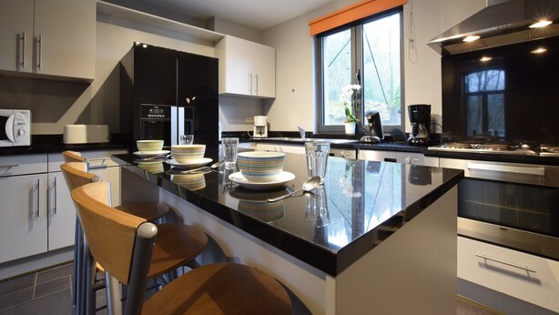 Una cocina moderna con una isla central, taburetes de bar y un ventanal con persiana naranja.