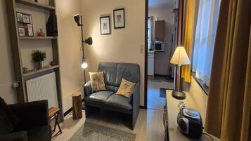 A living room with a sofa, a lamp, a small table with a radio, and a view into the kitchen.