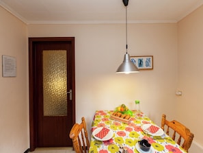 A dining area with a wooden table, chairs, a fruit basket, and a wall-mounted picture.