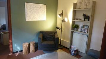 A living room with a grey armchair, a floor lamp, a bookshelf with decorative items, and a radiator.