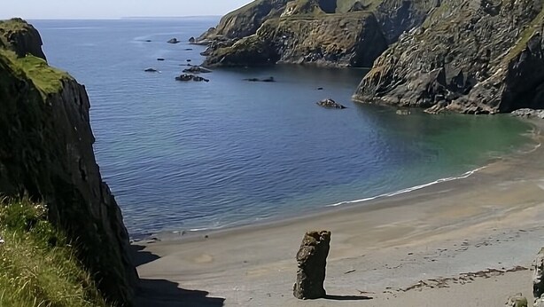 Un paisaje costero con una playa arenosa, acantilados rocosos y mar tranquilo.