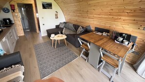 Una cocina acogedora y moderna con detalles de madera, un comedor con mesa y sillas de madera, y un espacio de sala con sofá y alfombra estampada.