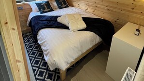 Una habitación cálida de madera con una cama, una mesita de noche pequeña y una ventana con cortinas.