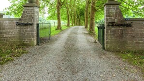 Een grindpad dat door een park slingert, met een bakstenen muur aan één kant en een metalen poort aan de andere kant.