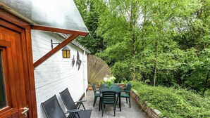 Een terras met een tafel en stoelen, een wit gebouw met een houten deur, en een bakstenen muur.