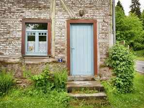 Un bâtiment en pierre avec une porte bleue et une fenêtre où l’on peut voir un journal.