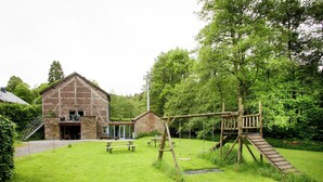 Une grange rustique avec une balançoire en bois et des tables de pique-nique, le tout situé dans une cour verdoyante.