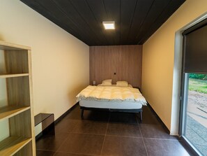 Ein kleiner, schmaler Raum mit einem Bett, einer Holzregaleinheit und einem Fenster.
