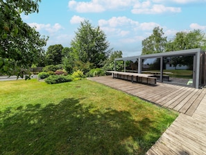 Eine moderne Terrassenanlage mit Glasverkleidung, Holzbanken und einem gepflegten Rasen.