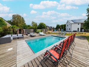 Ein Schwimmbecken mit Holzterrasse, Liegestühlen und einem modernen Haus im Hintergrund.