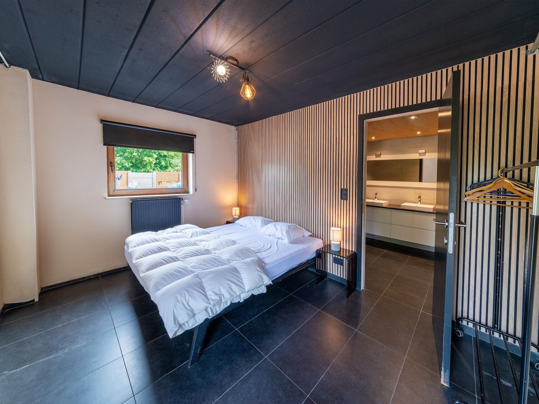 A modern bedroom with a large bed, a window, and a bathroom with a mirror and towel rack.