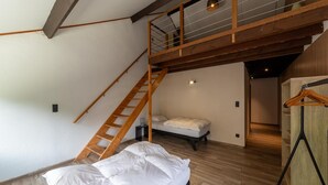A loft-style bedroom with a wooden ladder leading to a mezzanine, a single bed, and a wooden floor.