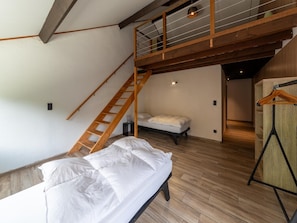 Ein Schlafzimmer im Loft-Stil mit einer Holzleiter zu einer Erker Ebene, einem Einzelbett und Holzboden.