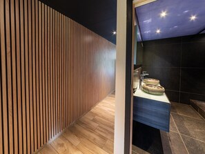 Ein modernes Badezimmer mit einer Wand aus Holzlatten, einem Waschbecken mit runder Spüle und dunklen Fliesenwänden.
