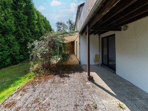 Ein Innenhof mit befestigtem Boden, einer Holzpergola und einer Glastür, die zu einem Raum führt.