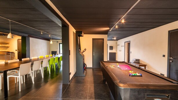 A modern interior with a pool table, a dining area with chairs, and a kitchen area.
