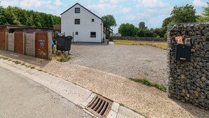 A gravel driveway leading to a white building with a metal gate and a stone wall with a mailbox.