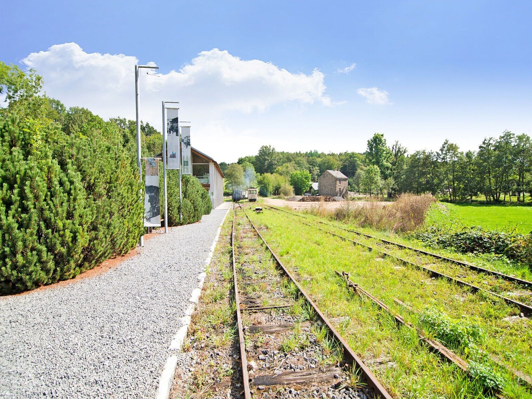 Une gare avec un chemin de gravier, plusieurs voies ferrées et un petit bâtiment en arrière-plan.