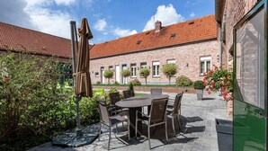 Eine Außenpatio mit einem runden Tisch und Stühlen, umgeben von Topfpflanzen und einem Backsteinhaus im Hintergrund.