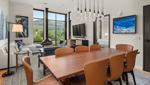 Une chambre d’hôtel moderne dotée d’une grande table à manger, de sièges confortables, d’une cheminée, d’une télévision et offrant une vue panoramique par les fenêtres.