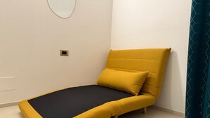 Una stanza piccola e moderna con un letto singolo, uno specchio rotondo a parete e una tenda color petrolio.