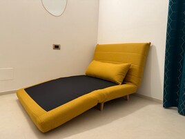 Una stanza piccola e moderna con un letto singolo, uno specchio rotondo a parete e una tenda color petrolio.