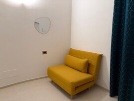 Un piccolo divano giallo in un angolo della stanza, con una parete bianca, uno specchio rotondo e una tenda blu scuro.