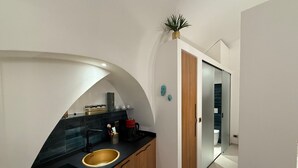 Una cucina moderna con un'isola a forma di curva, un lavello e una macchina da caffè. Si nota un armadietto in legno e una pianta sopra l'armadietto.