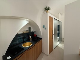 Una cucina moderna con un'isola a forma di curva, un lavello e una macchina da caffè. Si nota un armadietto in legno e una pianta sopra l'armadietto.