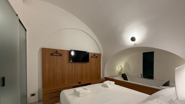 Una camera da letto moderna con una testiera in legno, una televisione a schermo piatto, uno specchio grande e letti rifatti con cura.
