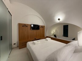 Una camera da letto moderna con una testiera in legno, una televisione a schermo piatto, uno specchio grande e letti rifatti con cura.