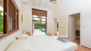 Ein Schlafzimmer mit einem großen Bett, Blick auf einen Swimmingpool und einer Tür zu einem Badezimmer.