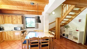 A spacious kitchen with wooden cabinets, a dining table with chairs, a microwave, and a staircase leading to an upper level. - Mountains Family Retreat (Rudník)