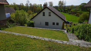 A white house with a stone pathway leading to it, surrounded by greenery and trees.