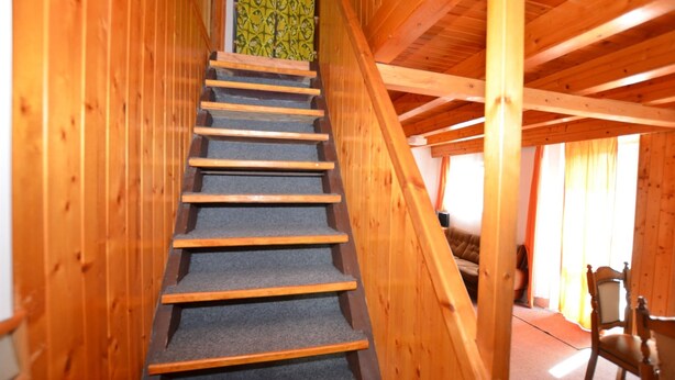 A wooden staircase with carpeted steps leading to a room with a sofa and a chair.