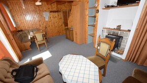 A cozy cabin interior with a sofa, a dining table with a checkered tablecloth, a wooden cabinet, and a fireplace.