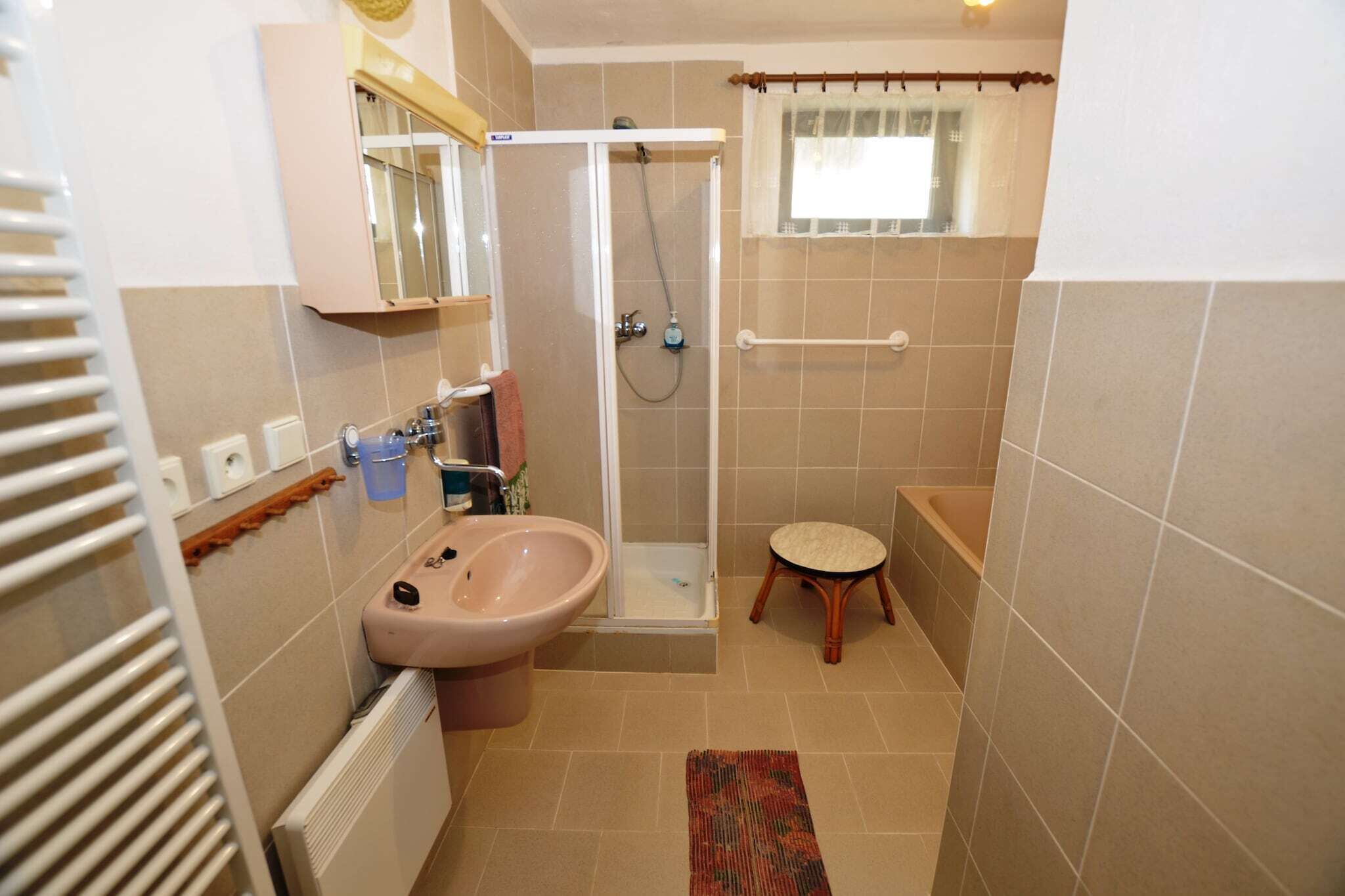 A compact bathroom with a shower, a sink, a toilet, and a small stool.